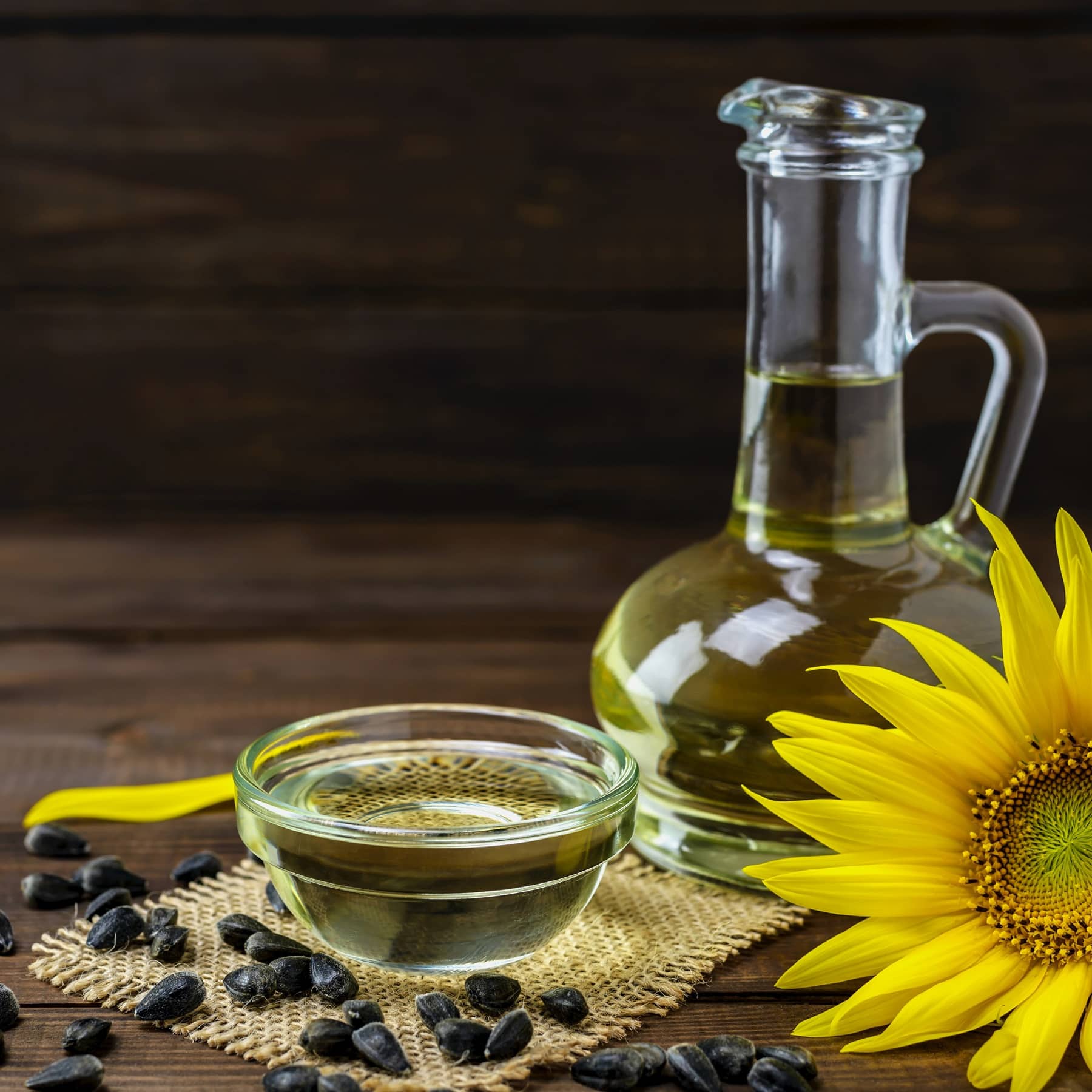 Sonnenblumenkerne und eine Pflanze auf einem Holztisch mit einem Schälchen Öl sowie einer Flasche mit Öl.