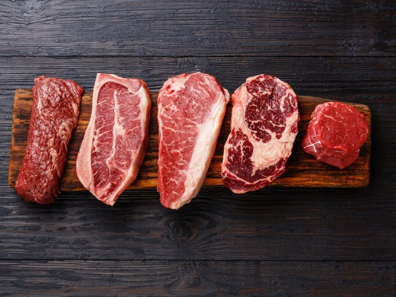 Welche Steaksorten gibt es verschiedene Steaks auf Holz und schwarzem Untergrund. Draufsicht.