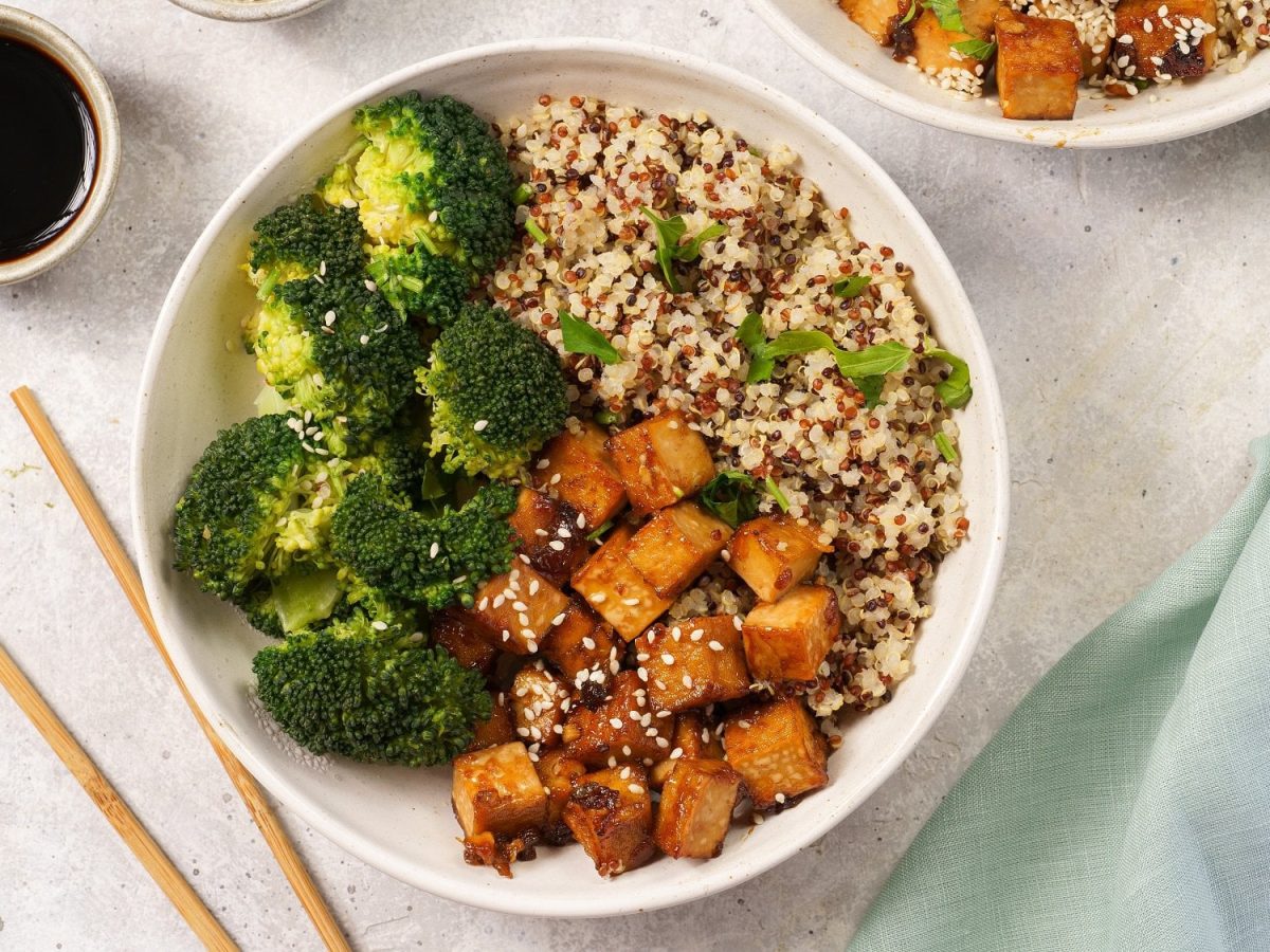 Eine Brokkoli-Quinoa-Bowl mit Tofu in der Draufsicht, daneben 2 Essstäbchen und eine Schale Sojasauce.