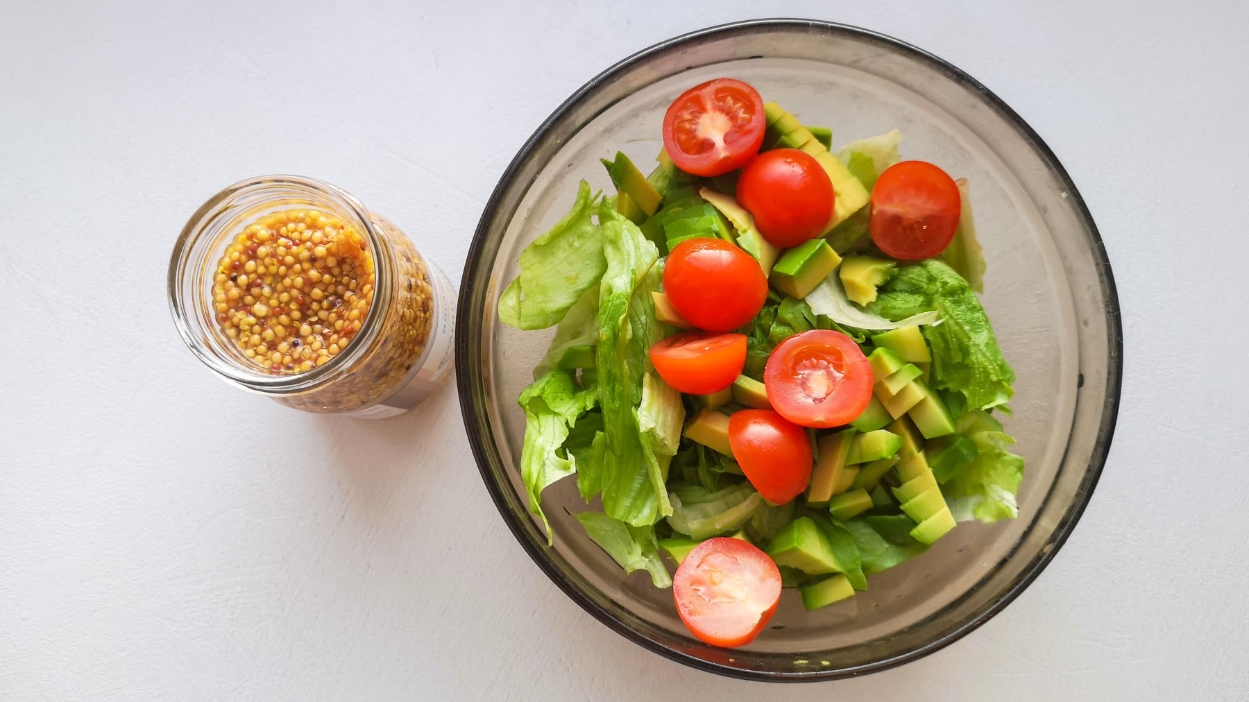 Senfkaviar in einem kleinen Glas. Rechts daneben eine Schüssel mit gemischten Salat. Der Hintergrund ist weiß.
