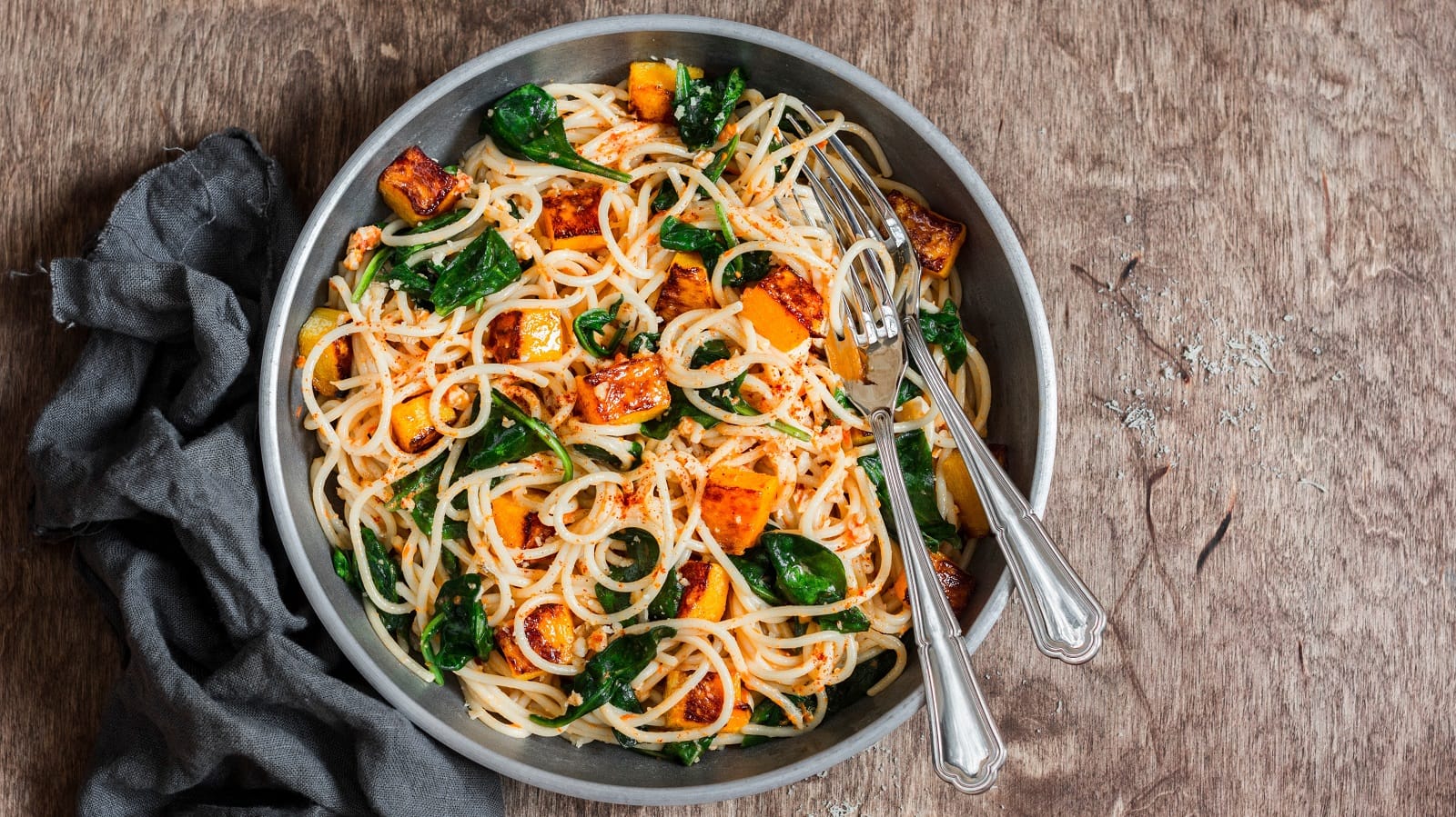 Ein Teller mit Kürbis-Pasta mit Spinat auf einem braunen Tisch.