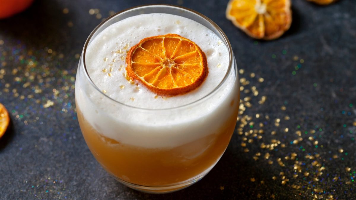 Ein Glas mit dem Drink auf einem dunklen tisch mit Glitzer und getrockneten Orangenscheiben.