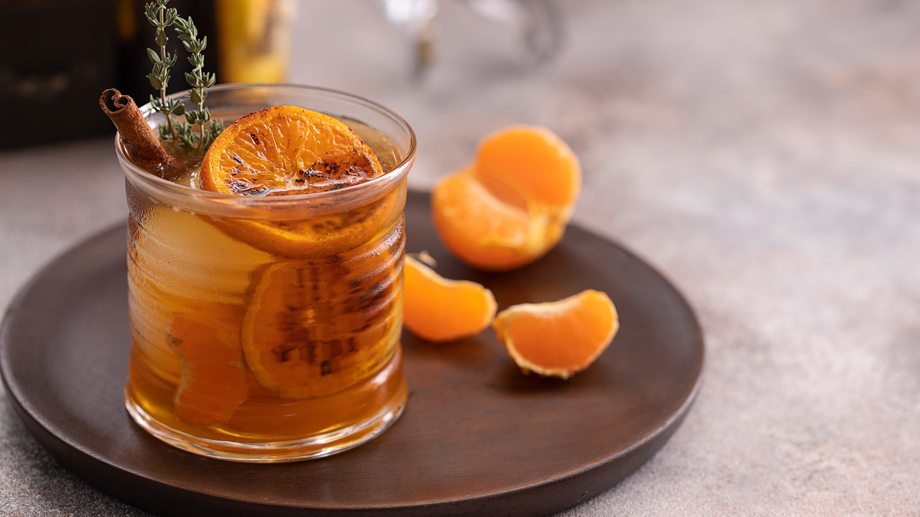 Ein Glas mit dem Drink auf einem braunen Teller mit Mandarinenstückchen.