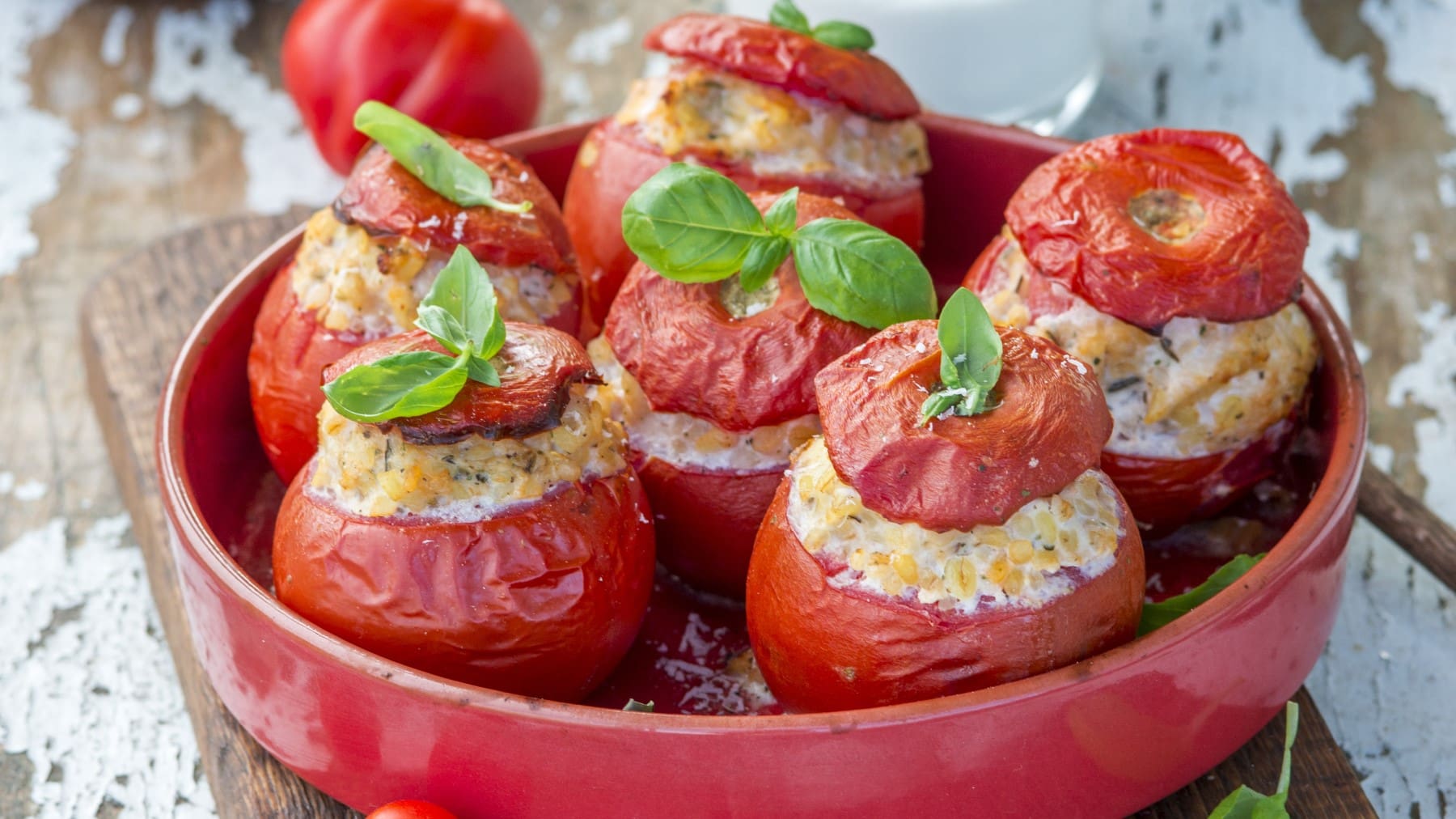 Fünf gefüllte Bulgur-Tomaten in einem roten tiefen Teller.