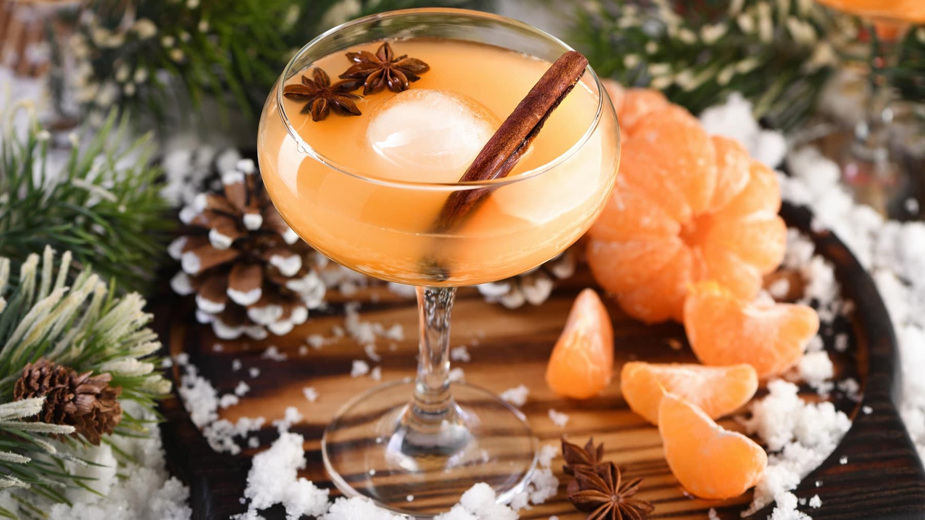Ein Glas mit dem Mandarinen Negroni auf einem dunklen Holztisch mit allerlei weihnachtlicher Dekoration.