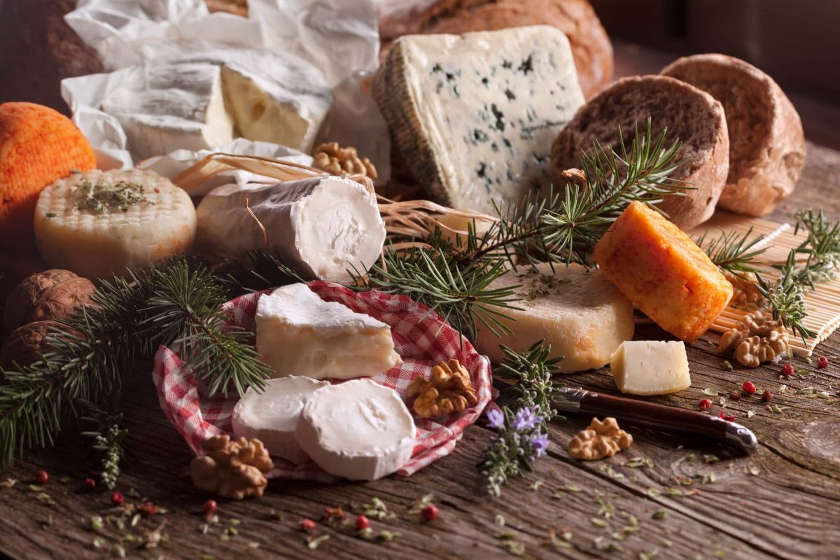 Frontal: eine Auswahl an Käsesorten liegen auf einem weihnachtlich geschmückten Holztisch. / perfekte Käseplatte