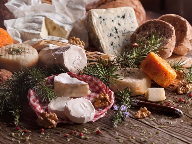 Frontal: eine Auswahl an Käsesorten liegen auf einem weihnachtlich geschmückten Holztisch. / perfekte Käseplatte