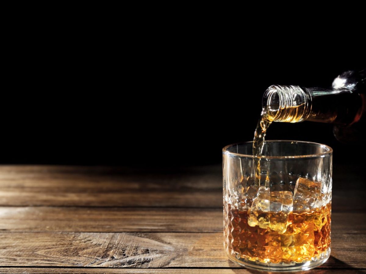 Whiskyglas vor dunklem Hintergrund, in das entweder Scotch oder Bourbon eingegossen wird.