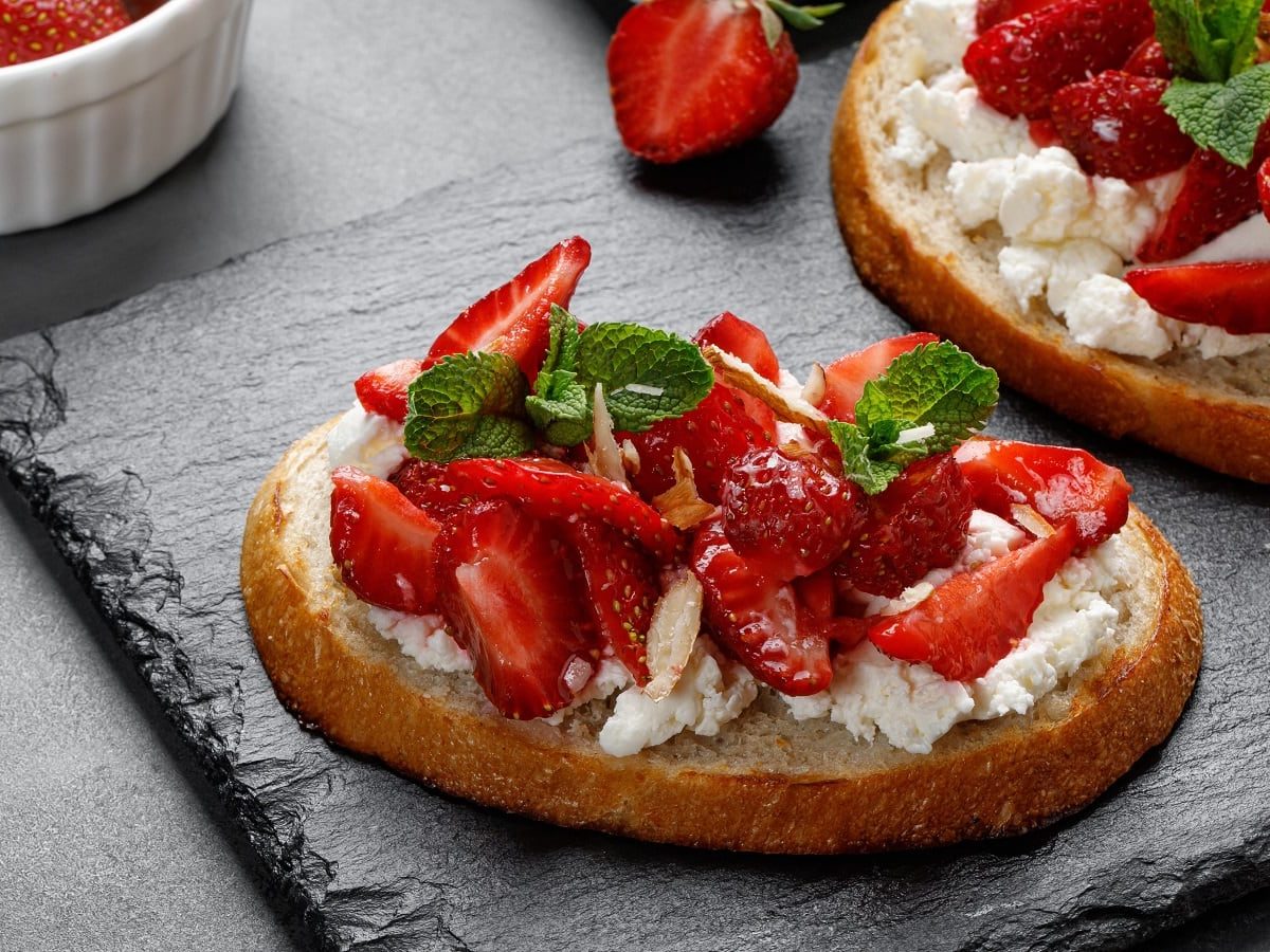 Ein Brot mit Cheesecake-Aufstrich und Erdbeeren auf einer Schieferplatte.