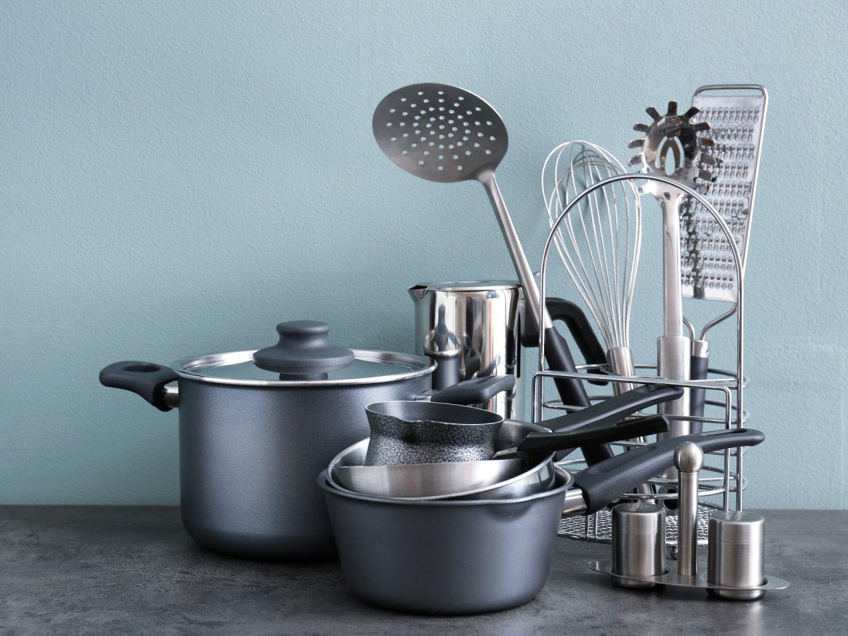 Eine Sammlung moderner Küchenutensilien in Grau und Silber, darunter Töpfe, Pfannen und Werkzeuge auf blaugrauem Hintergrund.