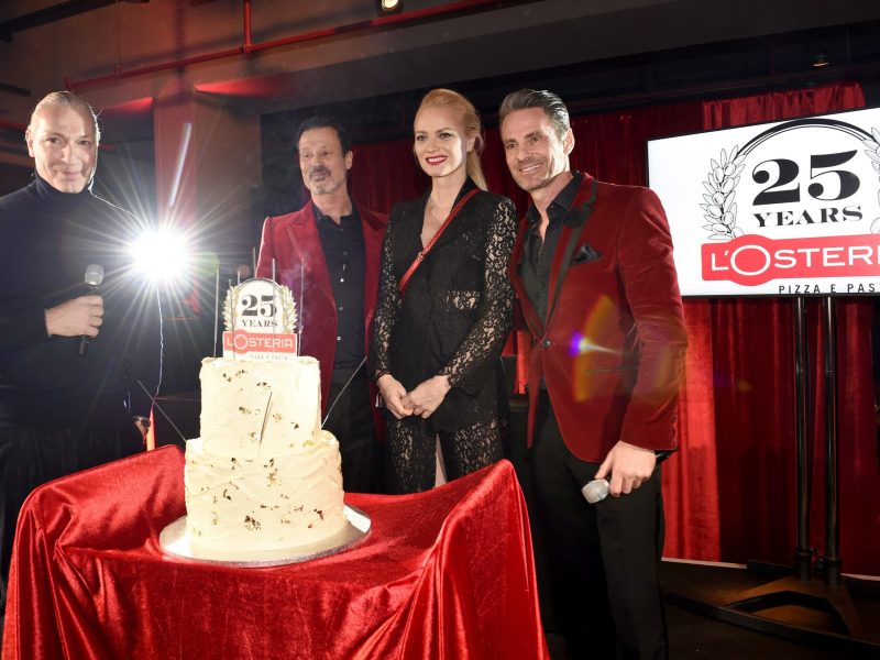 Die beiden Gründer mit Franziska Knuppe und der 25-jährigen Jubiläums-Torte auf einem roten Tisch. Alles direkt von vorne fotografiert.