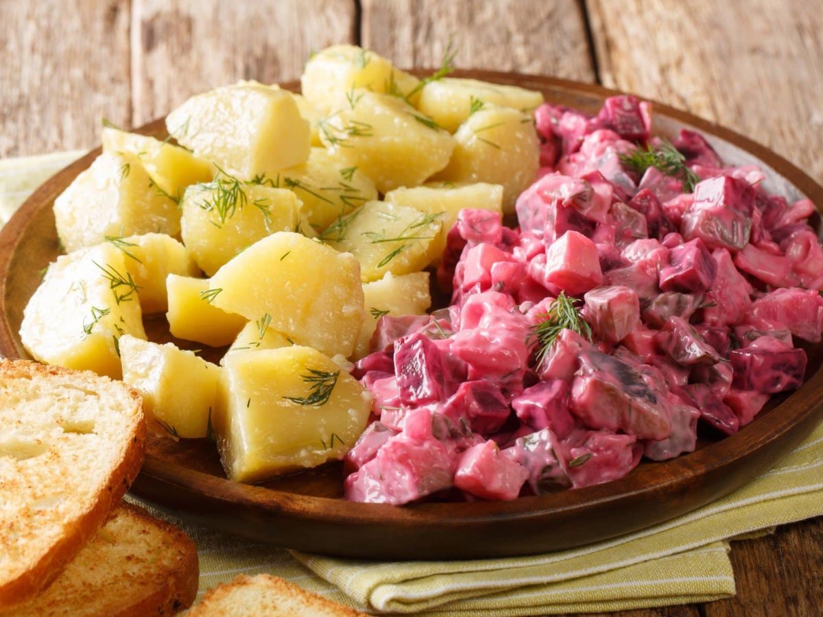 Draufsicht schräg: Ein Teller Roter Heringssalat mit Kartoffeln und gerösteten Weißbotscheiben.