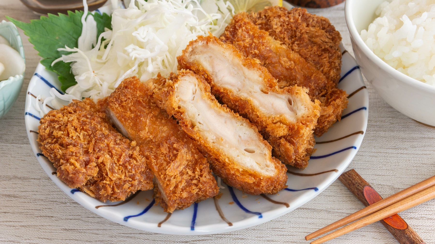 Geschnittenes Chicken Katsu mit Sprossen und Reis auf einem Teller.