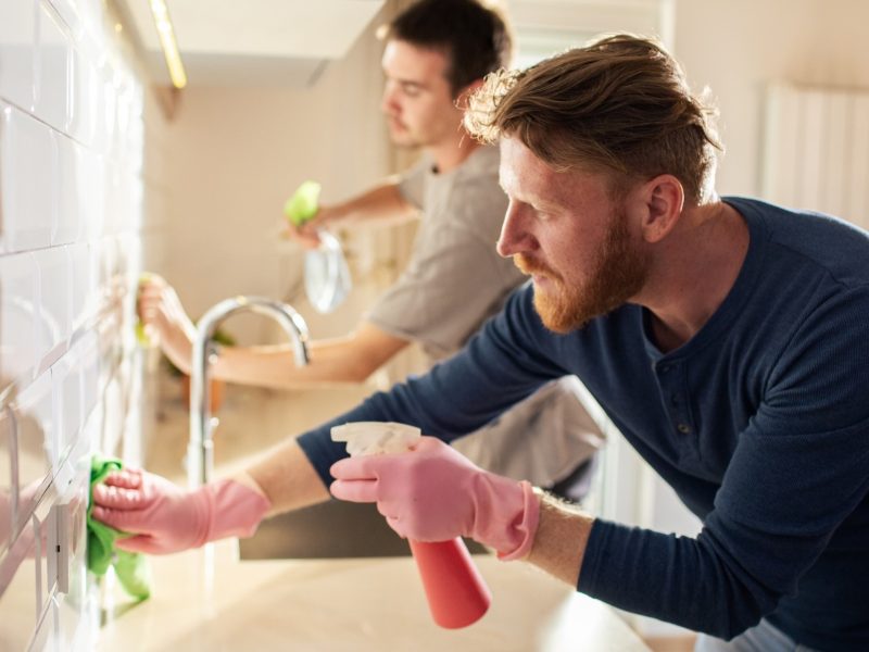 Frontal: Zwei Männer putzen eine Küche.