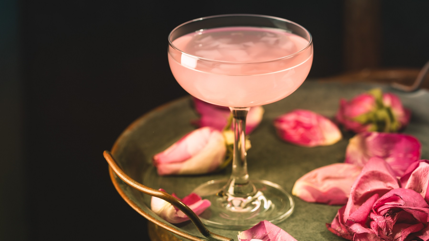 Cocktail mit Prosecco, schwarzen Tee und Rosengelee auf einem goldenen Tisch mit Rosenblättern