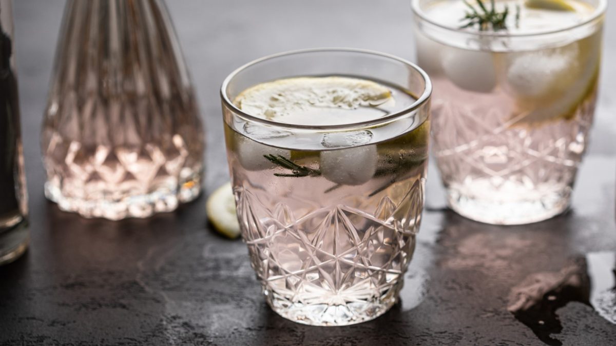 Zwei Gläser mit dem Wodka Wild Berry auf einem dunklen Tisch, mit weiteren Gläsern unscharf im Hintergrund. Alles recht nah und von der Seite fotografiert.