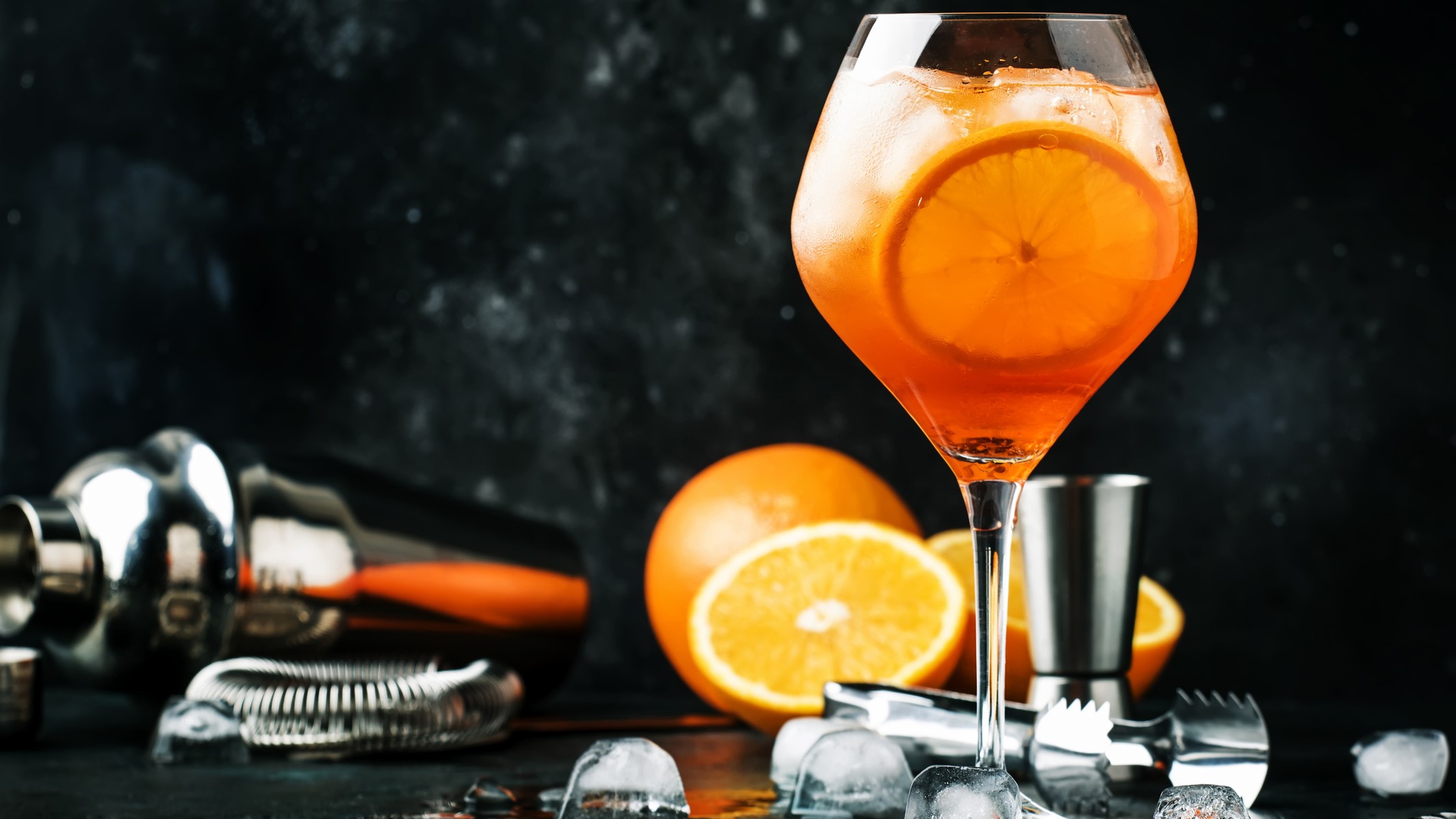 Aperol Spur in einem Glas. Im Hintergrund Orangen und Barzubehör.