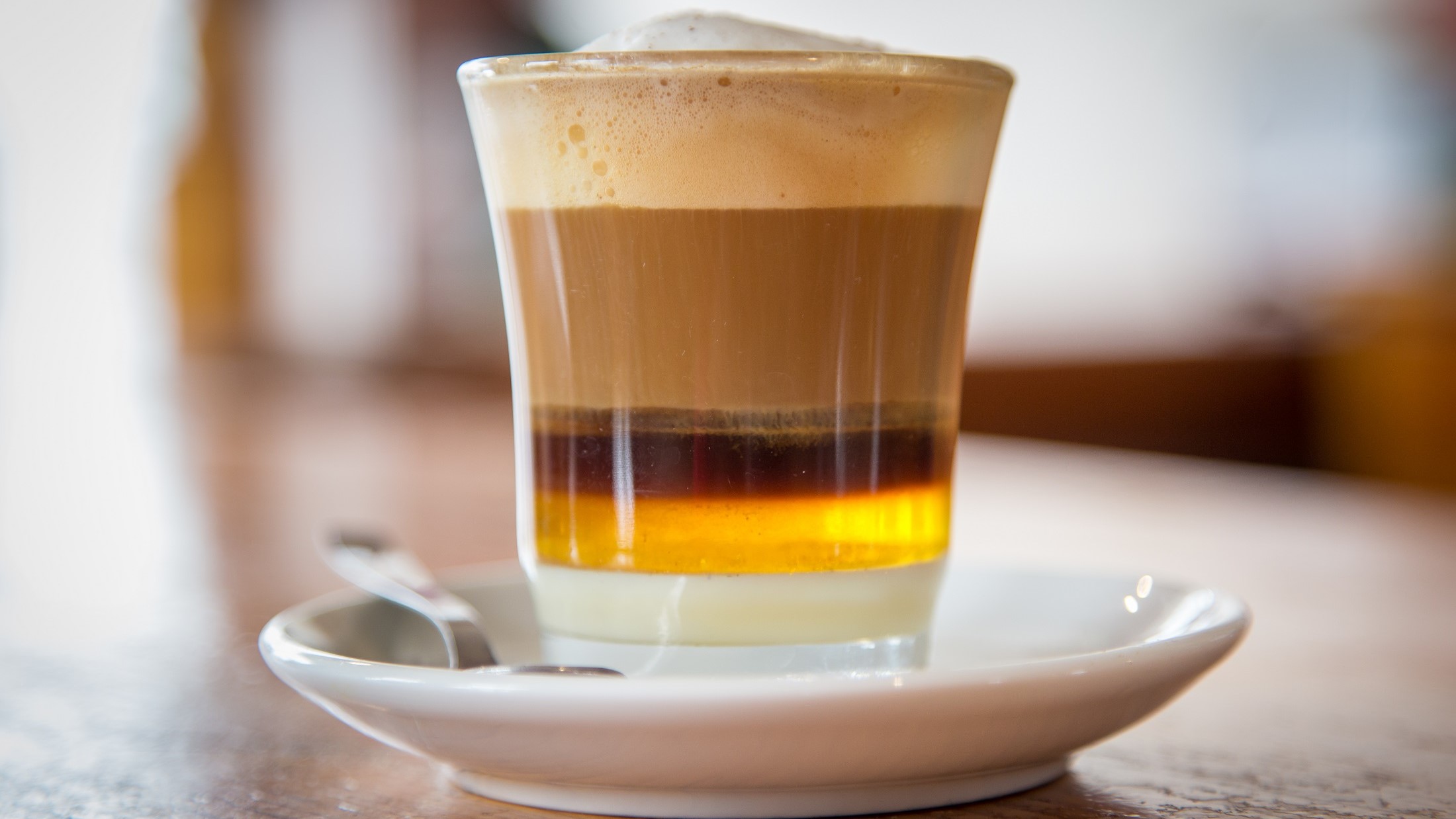 Frontal: Ein Glas mit einem Getränk, dass aus vielen Schichten besteht. Es handelt sich um eine spanische Kaffeespezialität von Teneriffa. Das Getränk heißt Barraquito.