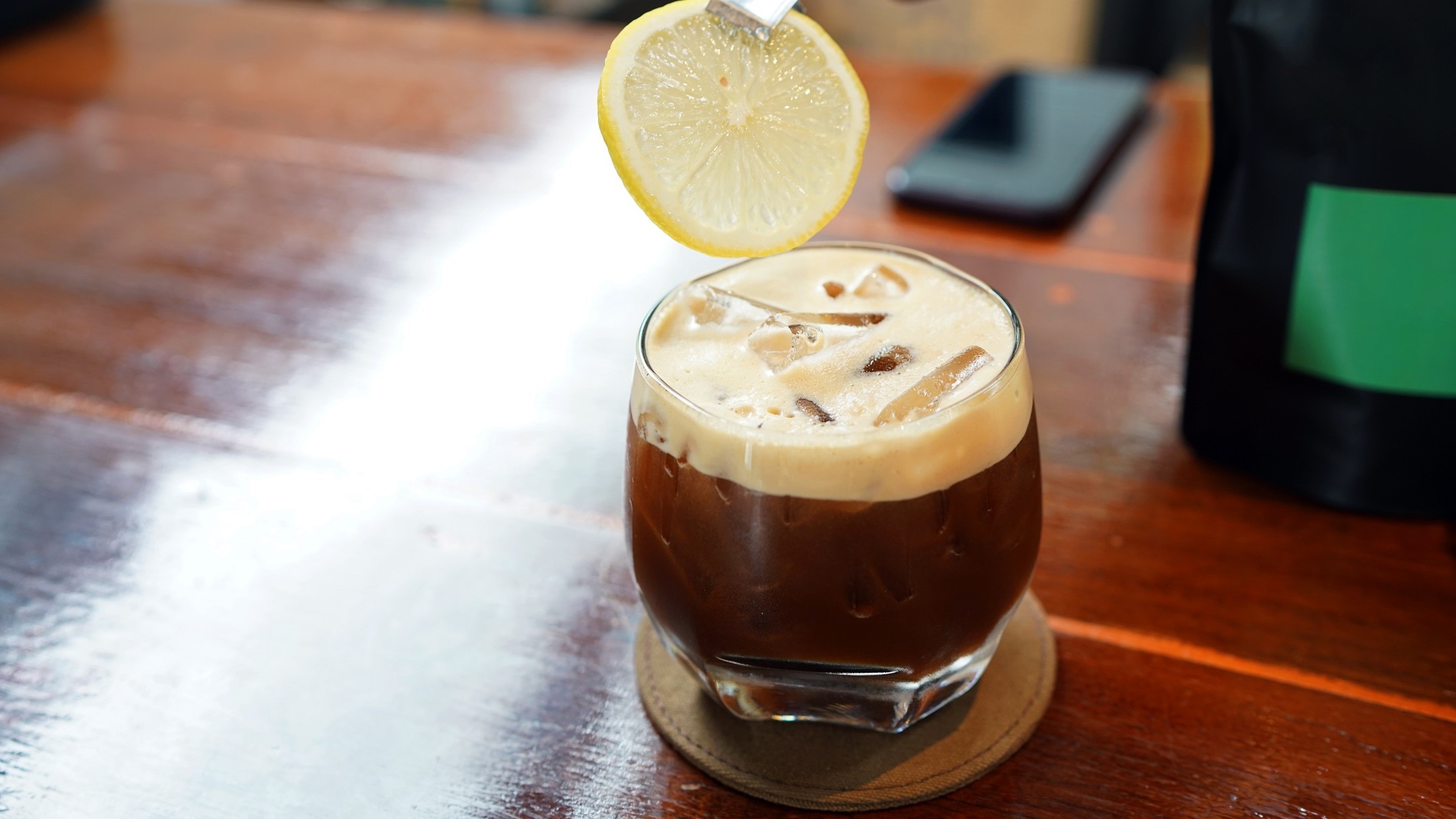 Draufsicht schräg: Ein Glas Golden Moment. In dem Kaffee-Cocktail ist eine Scheibe Zitrone.