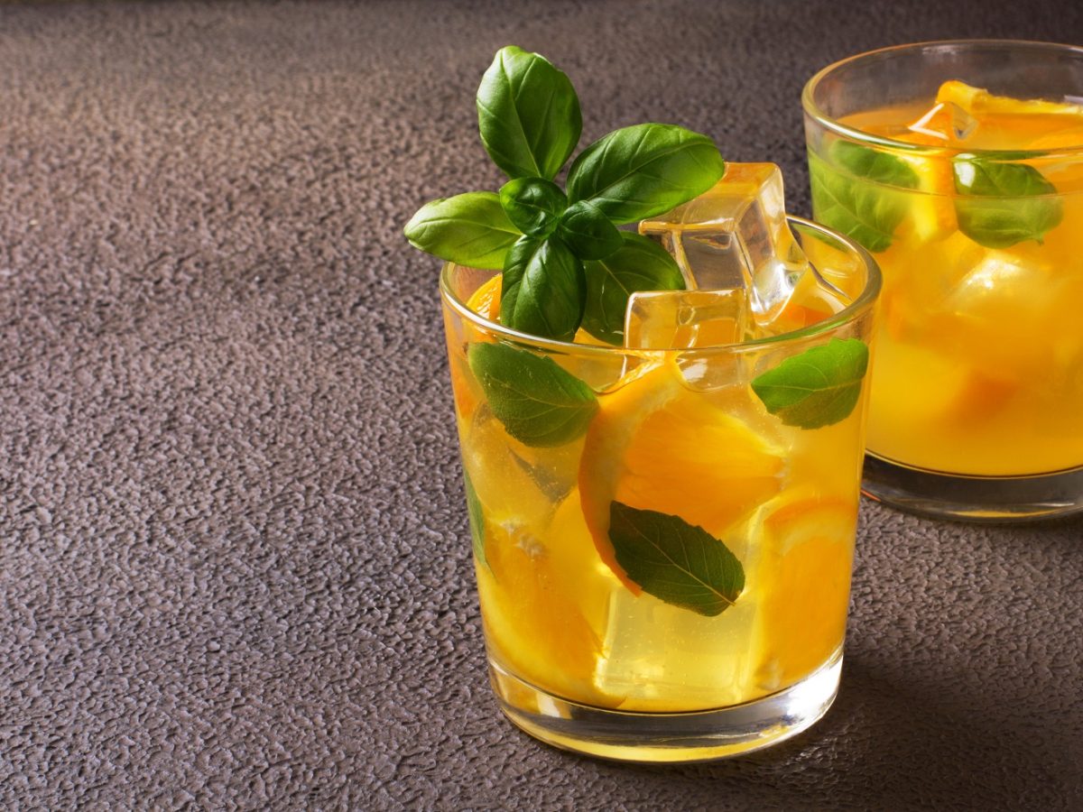 Orangen-Basilikum-Limonade in zwei Gläsern, garniert mit Basilikumblättern und Eiswürfeln.