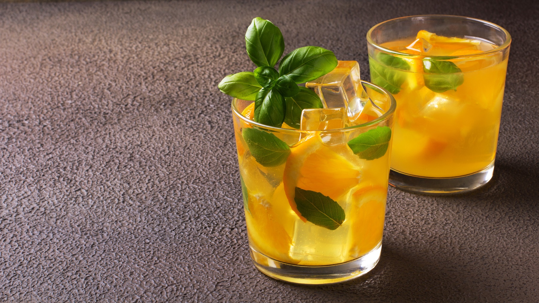 Orangen-Basilikum-Limonade in zwei Gläsern, garniert mit Basilikumblättern und Eiswürfeln.
