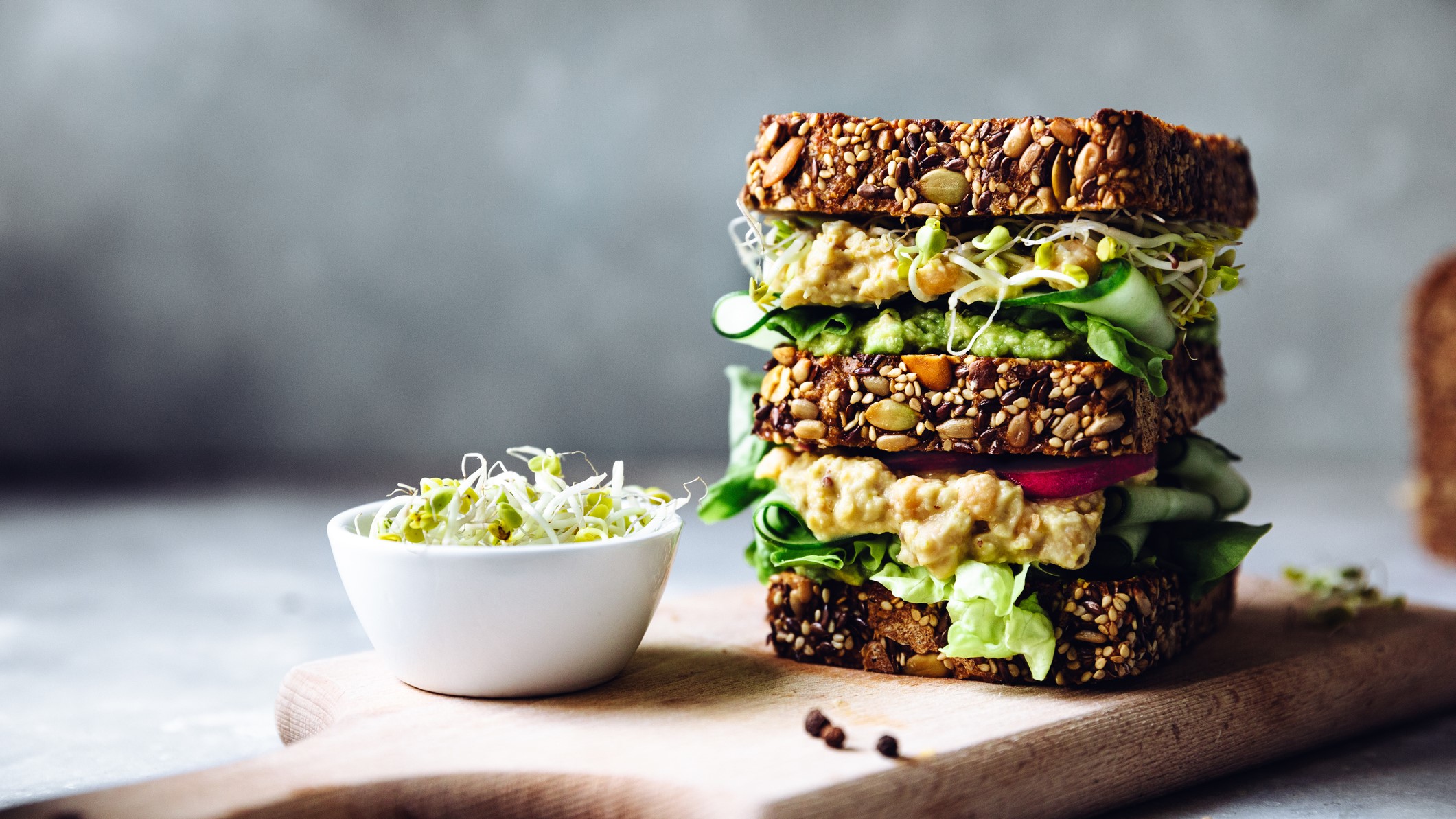 Veganes Sandwich mit Kichererbsensalat und Sprossen auf einem Brett.
