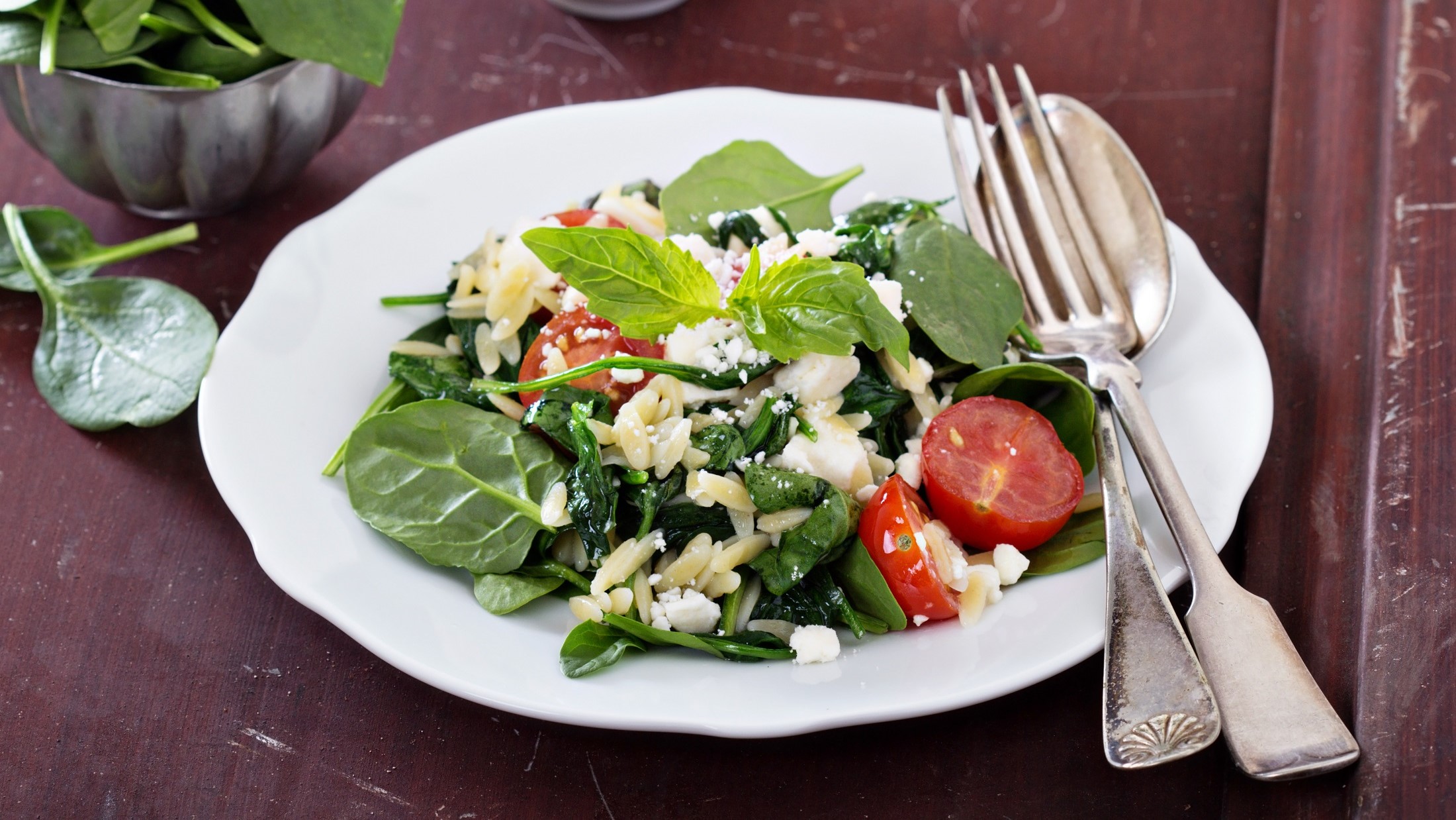 Draufsicht, schräg: Ein weißer Teller mi Orzo-Spinat-Salat.