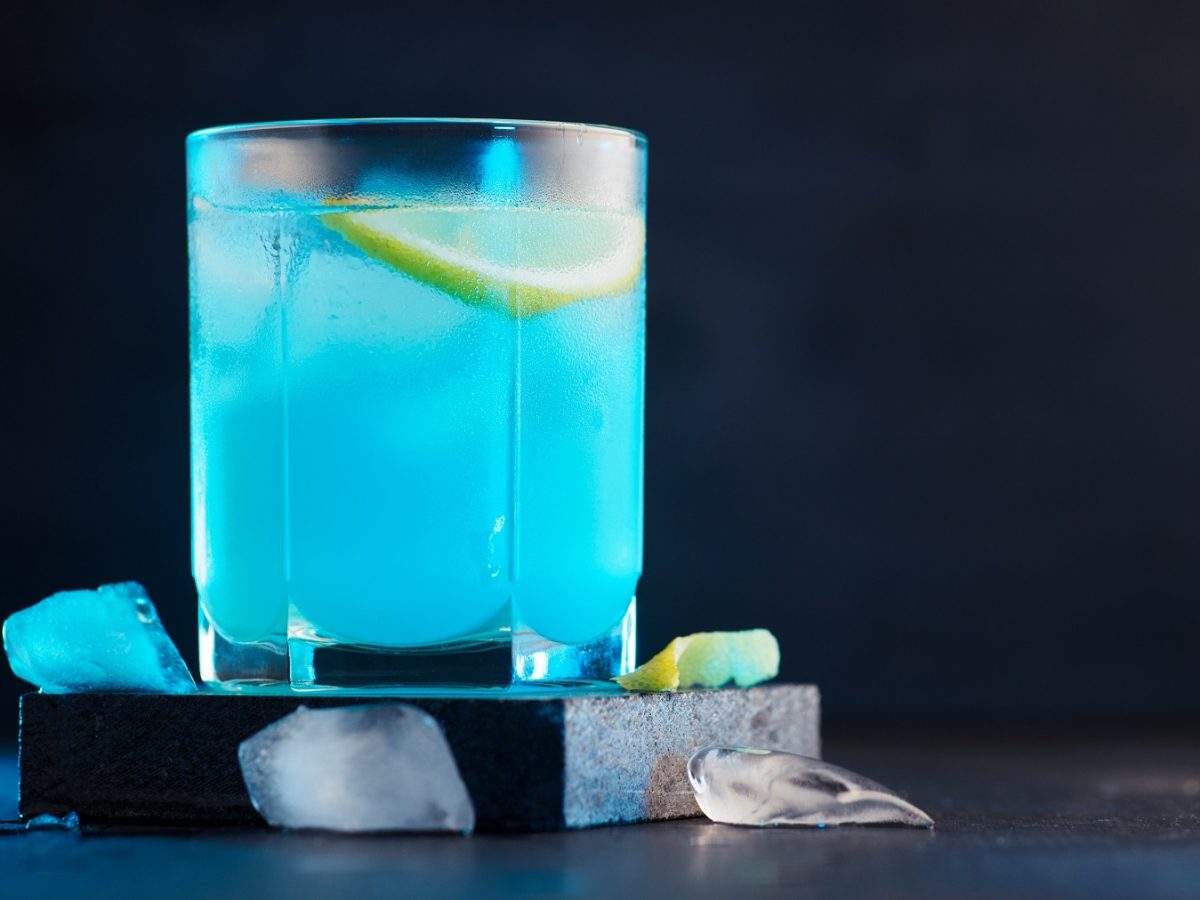 Ein Glas mit dem türkis-blauen Cocktail auf dunklem Untergrund und schwarzem Hintergrund.